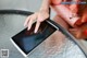 A woman is touching a tablet computer on a table.