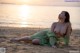 A woman in a green dress sitting on the beach.