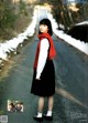 A woman in a black dress and red scarf standing on a road.